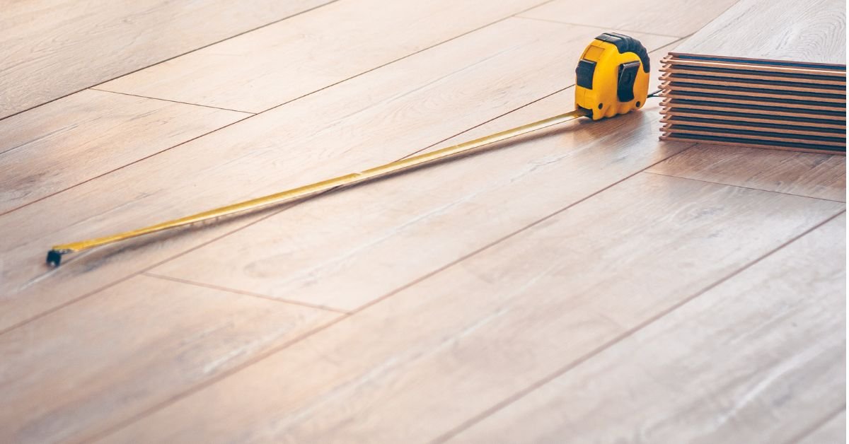 A yellow tape measure rests on a wooden floor, showcasing its length and flexible design.
