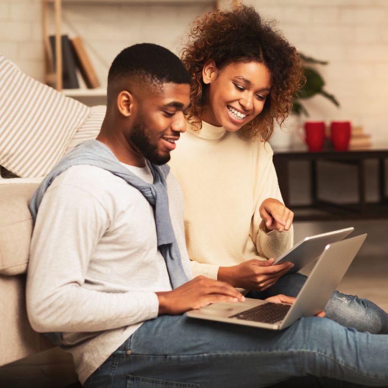 A young couple sitting together on a couch, using a laptop in their cozy living room.