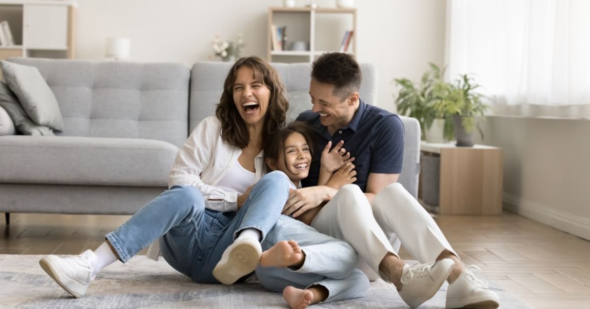 A joyful family sitting on the floor, laughing and smiling together, creating a warm and happy atmosphere.