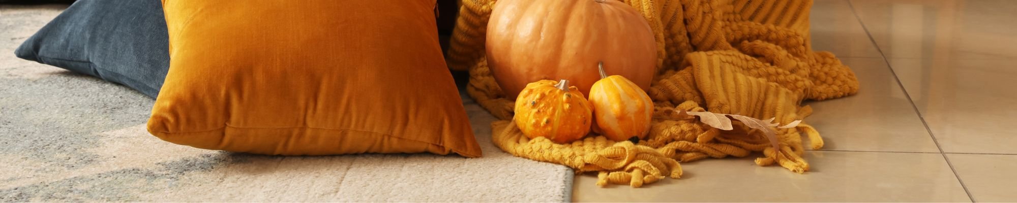 A vibrant assortment of pillows stacked on the floor next to a decorative pumpkin.