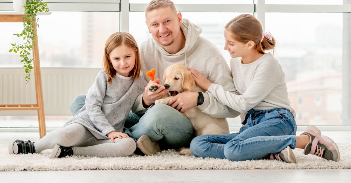 A man and two children sit on the floor, playing with a dog, creating a joyful family moment.