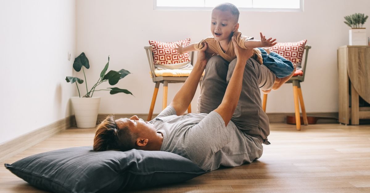 A man and a child are joyfully playing together on the floor, surrounded by toys and a warm, inviting atmosphere.