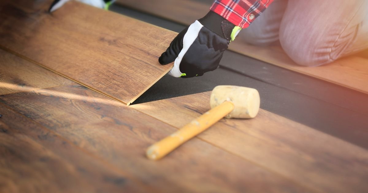 A person installing wood flooring by hammering down planks on a wooden subfloor.