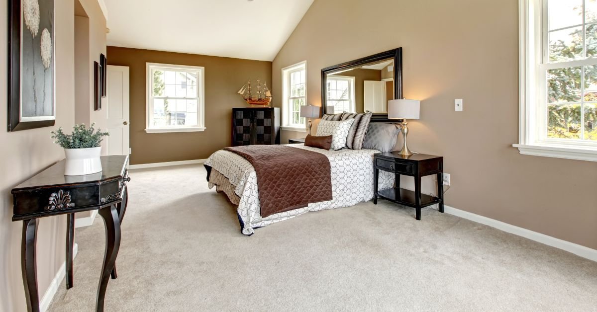 A cozy bedroom featuring a neatly made bed, a wooden dresser, and a wall-mounted mirror reflecting the room's decor.